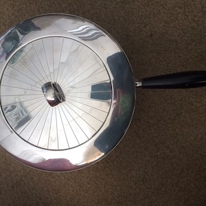 May include: A silver serving dish with a black handle. The dish has a circular, ridged design.