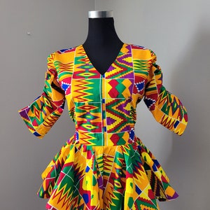 May include: A colourful, patterned dress with a V-neck and short sleeves. The dress has a fitted bodice and a flared skirt. The fabric is a vibrant yellow, red, green, and purple.
