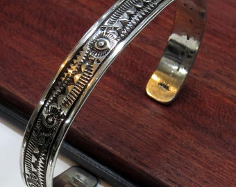May include: A silver bracelet with a geometric pattern. The bracelet is made of a smooth, polished metal and has a simple, elegant design.