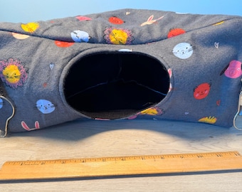 May include: A gray pet tunnel bed with a large opening and colorful cartoon animal designs. The bed has a rectangular shape and is approximately 12 inches long. It features a handle and a metal ring for hanging.