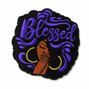 May include: An embroidered patch with a black background featuring a brown-skinned face with eyes closed and hands near the mouth. The word Blessed is stitched in purple script above the face, surrounded by purple swirls and yellow hoop earrings.