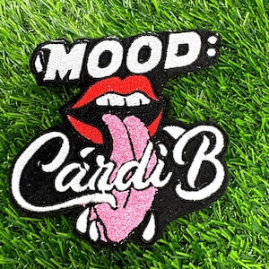 May include: Embroidered patch with the words "MOOD:" above a graphic of red lips with a pink tongue sticking out. Below the lips is the name "Cardi B" in white script. The patch is on a black background.