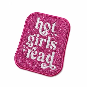 May include: A rectangular embroidered patch with rounded corners featuring a vibrant hot pink glittery background. The text "hot girls read" is stitched in a white, cursive-style font across the center, accented by small white star details.