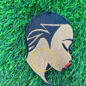 May include: Embroidered iron-on patch featuring a profile of a person with short black hair, brown skin, and a gold hoop earring. The person is wearing red lipstick.