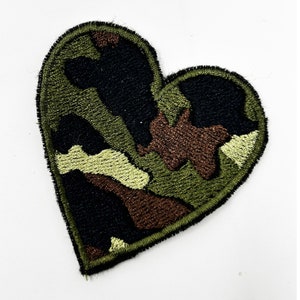 May include: A green, brown, and black camouflage heart-shaped patch. The patch is made of embroidered fabric.