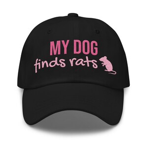 Peut inclure: Une casquette de baseball noire avec le texte rose brodé MY DOG finds rats et un petit graphique rose représentant la silhouette d'un rat. Le motif est centré sur le panneau avant de la casquette, qui possède une visière courbée et une calotte structurée.