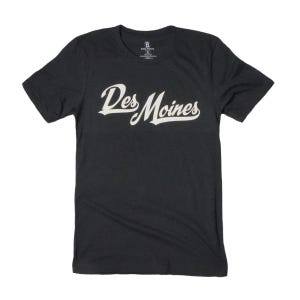 May include: Dark gray t-shirt with the text "Des Moines" in a white, cursive font. The shirt has short sleeves and a crew neck. A small logo is visible near the neckline.