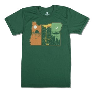 Peut inclure: Un t-shirt vert avec un graphique représentant l'état de l'Oregon, avec un coucher de soleil, une cascade et une lune. Le graphique est dans des tons d'orange, de jaune et de vert.