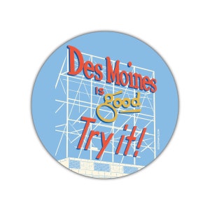 Könnte beinhalten: Ein blauer und weißer runder Aufkleber mit dem Text "Des Moines is good Try it!" in roten und gelben Buchstaben. Der Aufkleber zeigt eine stilisierte Illustration einer Werbetafel mit einer Skyline der Stadt im Hintergrund.