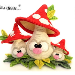 Könnte beinhalten: Drei gehäkelte Pilz-Amigurumi-Spielzeuge mit roten und weißen Hüten und weißen Augen. Die Pilze sitzen auf einem Bett aus grünen gehäkelten Blättern.