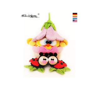 Puede incluir: Un pollito de crochet en una maceta de flores rosa con dos mariquitas rojas y negras. El pollito tiene plumas amarillas, ojos negros y una corbata de lazo rosa. Las mariquitas tienen manchas negras y caras blancas.