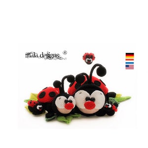 Può includere: Una famiglia di cinque coccinelle all'uncinetto in rosso, nero e bianco, sedute su foglie verdi. Le coccinelle hanno occhi neri e punti rossi. La coccinella più grande è al centro, con due coccinelle più piccole su entrambi i lati e due coccinelle ancora più piccole alle estremità.
