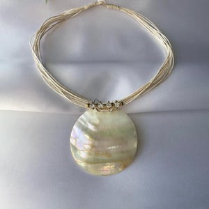 May include: A white ceramic mug with a black handle and the text "But First, Coffee" in a bold, black font. The mug is set against a blurred background, suggesting a cozy setting.