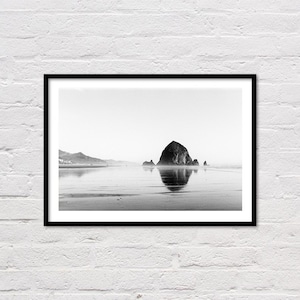 Könnte beinhalten: Ein Schwarzweißfoto einer großen Felsformation im Meer, mit einer Reflexion des Felsens im Wasser.