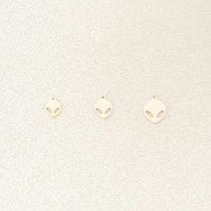 Può includere: Tre ciondoli a forma di testa aliena dorati di diverse dimensioni. I ciondoli sono ritagliati in metallo e hanno una finitura liscia e lucida.