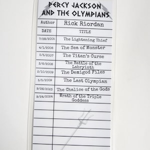 May include: A white and black checklist with the title "Percy Jackson and the Olympians" and a list of book titles and publication dates. The author is listed as Rick Riordan. The checklist also includes a drawing of a trident and the words "Camp Half-Blood".