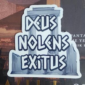 Puede incluir: Una pegatina blanca con la frase latina "Deus Nolens Exitus" en letras azules estilizadas. El dise&ntilde;o incorpora elementos arquitect&oacute;nicos como columnas y un templo, sobre un fondo de portada de libro.