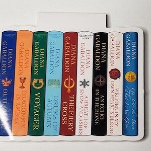 May include: A set of ten Outlander book covers featuring the titles "Outlander", "Dragonfly in Amber", "Voyager", "Drums of Autumn", "The Fiery Cross", "A Breath of Snow and Ashes", "An Echo in the Bone", "Written in My Own Heart's Blood", and "Go Tell the Bees That I Am Gone".