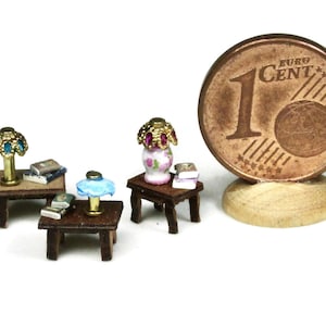 May include: Three miniature wooden tables with lamps and books. The tables are dark brown with a light brown top. The lamps are gold with blue and pink shades. The books are stacked on top of the tables. A 1 Euro cent coin is included for scale.