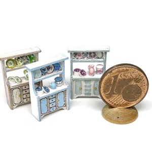 Könnte beinhalten: Drei weiße, bemalte Miniaturschränke mit blauen Verzierungen und Regalen. Die Schränke sind mit Miniaturtellern und Geschirr gefüllt. Eine Ein-Euro-Münze ist zur Größenbestimmung enthalten.