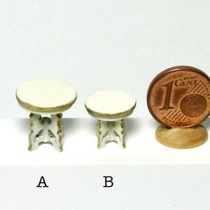 May include: Two white miniature tables with gold trim and ornate legs. The table on the left is slightly larger than the table on the right. A 1 Euro cent coin is included for scale.
