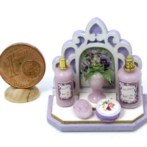 May include: A miniature purple and white bathroom vanity set with three bottles of lavender-scented toiletries, a bar of soap, and a decorative floral lidded box. The bottles have labels that read "Paris Vienna" and "Violet Oil".