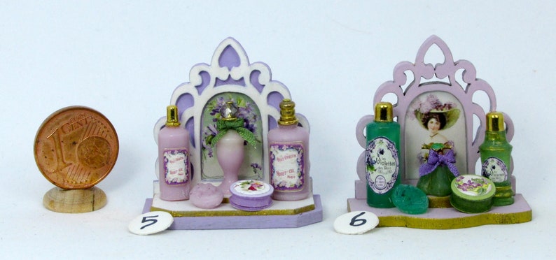 May include: Two miniature bathroom sets with decorative mirrors, bottles, and soap dishes. The set on the left is lavender and white with a floral design. The set on the right is green and white with a woman in a hat and dress.