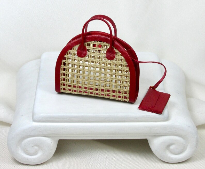 K&ouml;nnte beinhalten: Eine rote geflochtene Handtasche mit einem oberen Henkel und einer passenden roten Tasche. Die Tasche hat ein geflochtenes Strohmuster und einen Lederbesatz.