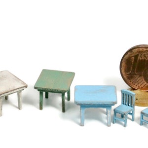 Puede incluir: Cuatro mesas de madera en miniatura de color blanco, verde y azul, con dos sillas azules a juego. Las mesas son todas cuadradas y tienen diseños simples. Las sillas también son simples y tienen un respaldo de listones.