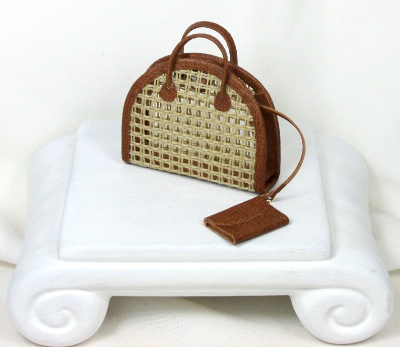 K&ouml;nnte beinhalten: Eine kleine braune geflochtene Handtasche mit einem Ledergriff und einer passenden Ledertasche. Die Tasche hat eine abgerundete Form und ein geflochtenes Design.