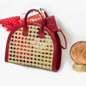 K&ouml;nnte beinhalten: Eine rote geflochtene Handtasche mit einem braunen Ledergriff und einem rot-wei&szlig; gepunkteten Schal im Inneren. Die Tasche ist etwa so gro&szlig; wie eine Ein-Euro-M&uuml;nze.