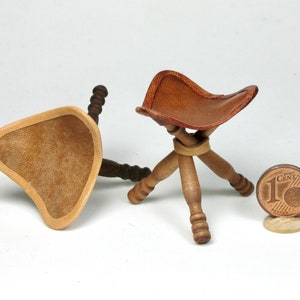 Könnte beinhalten: Zwei Miniatur-Hocker aus Holz mit braunen Ledersitzen. Die Hocker sind aus Holz gefertigt und haben ein schlichtes Design. Die Hocker sind etwa so groß wie eine deutsche Ein-Cent-Münze.
