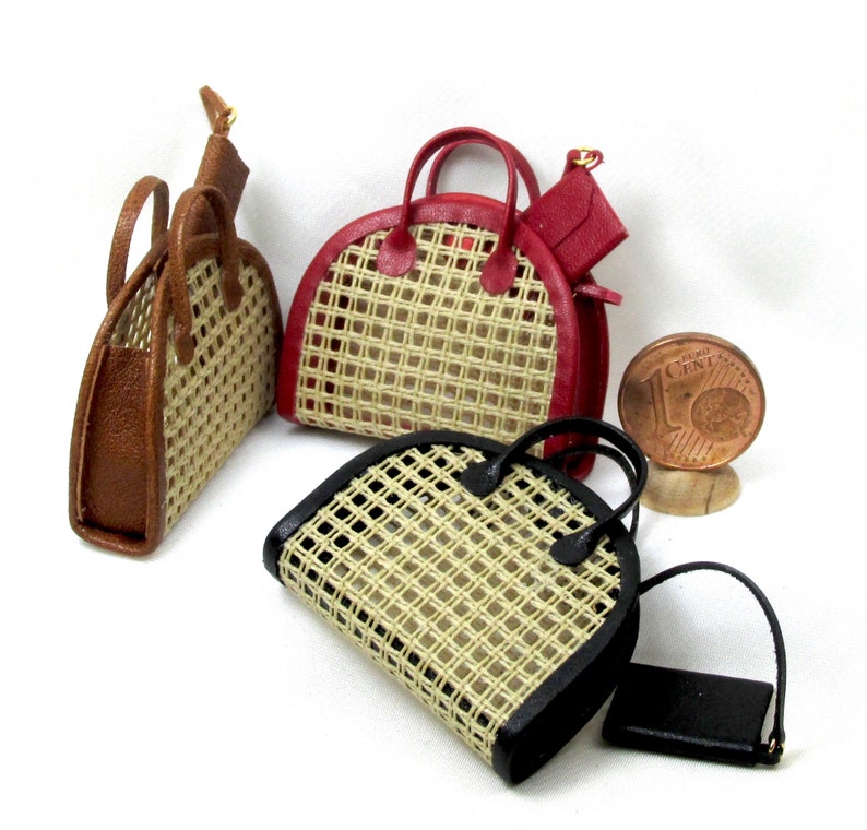 K&ouml;nnte beinhalten: Drei Miniatur-Handtaschen mit geflochtenen Stroheins&auml;tzen und Lederbesatz. Die Handtaschen sind braun, rot und schwarz.