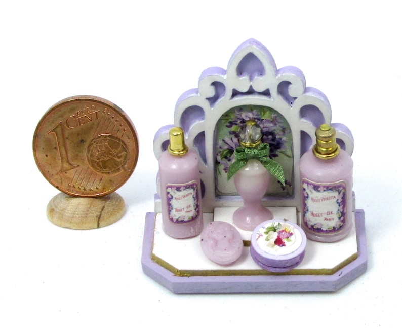 May include: A miniature purple and white bathroom vanity set with three bottles of lavender-scented toiletries, a bar of soap, and a decorative floral lidded box. The bottles have labels that read "Paris Vienna" and "Violet Oil".