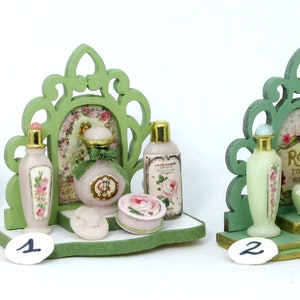 May include: Two miniature green wooden shelves with decorative cutouts, each holding a collection of miniature bottles of perfume and soap. The shelves are decorated with floral patterns and the bottles have labels with floral designs and text.