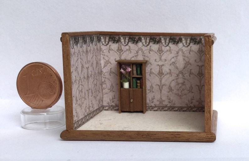 May include: A miniature dollhouse room with a wooden bookcase with glass doors and shelves filled with books. The bookcase is in front of a wallpapered wall with a floral pattern. The room is empty except for the bookcase.