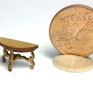 Może przedstawiać: Miniaturowy drewniany stolik w kształcie półksiężyca z misternymi rzeźbami na nogach. Stolik jest mniej więcej wielkości polskiej monety jednogroszowej.