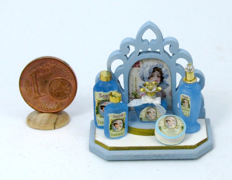 May include: A miniature blue vanity set with a mirror, four bottles of blue liquid, and a round jar of cream. The bottles and jar have labels with the word "Salvo" and a woman's face. The set is on a blue wooden base.