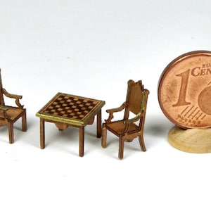 May include: A miniature wooden chess table set with two chairs. The table has a checkered top and a gold trim. The chairs have a high back and carved details. The set is about the size of a 1 Euro cent coin.