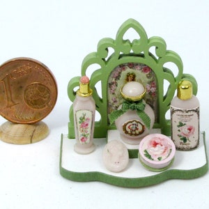 May include: A miniature dollhouse bathroom set with a green wooden frame, a pink and white floral patterned bottle, a pink and white floral patterned soap dish, a pink and white floral patterned bottle of soap, and a pink and white floral patterned bottle of perfume.