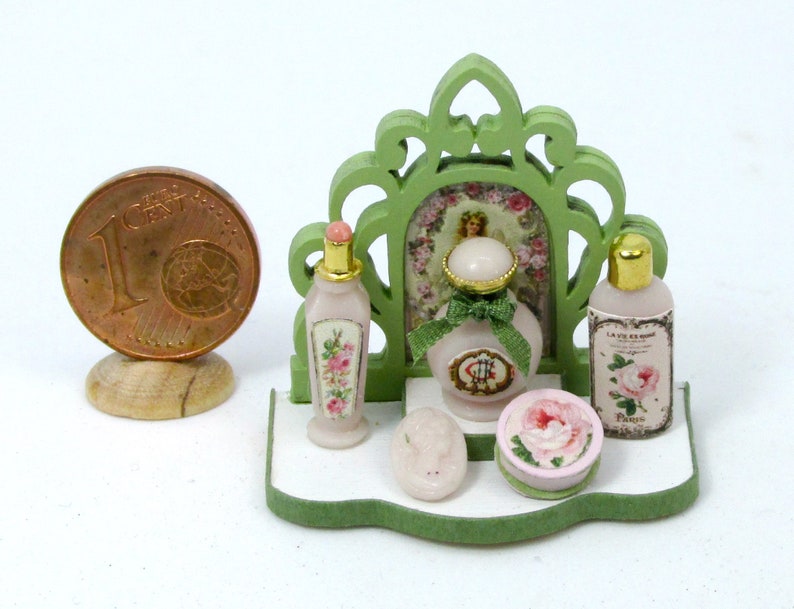 May include: A miniature dollhouse bathroom set with a green wooden frame, a pink and white floral patterned bottle, a pink and white floral patterned soap dish, a pink and white floral patterned bottle of soap, and a pink and white floral patterned bottle of perfume.