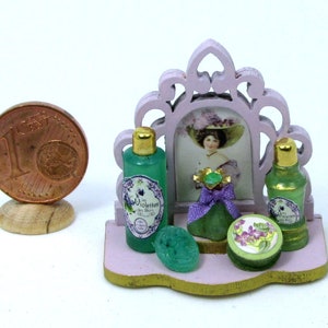 May include: A miniature vanity set with a pink frame mirror, two green glass bottles with labels that say "Violettes", a green glass bottle with a purple ribbon, and a green soap dish with a floral design.