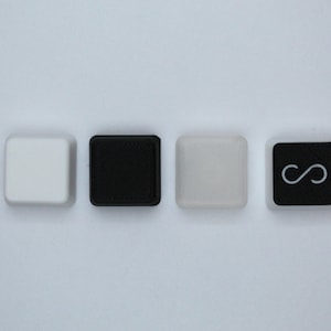 May include: Four square keys with different colors and symbols. The first key is white, the second is black, the third is light gray, and the fourth is black with a white infinity symbol.