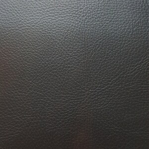 May include: Close-up of a black leather texture with a subtle sheen. The leather has a pebbled surface, creating a textured look.