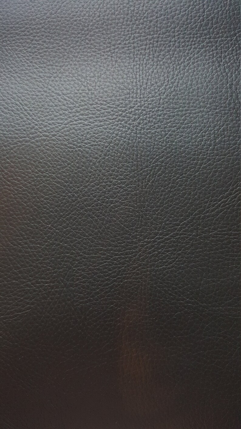 May include: Close-up of a black leather texture with a subtle sheen. The leather has a pebbled surface, creating a textured look.