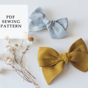 May include: Two fabric hair bows, one light blue and one mustard yellow, on a white background. The text "PDF SEWING PATTERN" is in a white box above the bows.