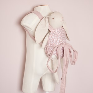 Peut inclure: Un porte-b&eacute;b&eacute; floral rose et blanc avec une poup&eacute;e lapin attach&eacute;e. Le porte-b&eacute;b&eacute; a de longues attaches qui peuvent &ecirc;tre nou&eacute;es autour de la taille.