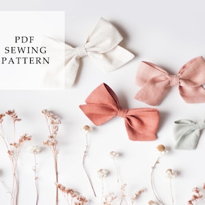 Può includere: Quattro fiocchi per capelli in tessuto di diversi colori: bianco, rosa chiaro, corallo e verde chiaro. I fiocchi sono disposti su uno sfondo bianco con fiori secchi. Il testo "PDF SEWING PATTERN" è in una casella bianca.