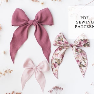Op de afbeelding: Drie stoffen haarbandjes, een roze, een bordeauxrood en een met bloemenprint. De strikken zijn op een witte achtergrond met gedroogde bloemen gerangschikt. De tekst "PDF SEWING PATTERN" staat in een wit kader in de rechterbovenhoek van de afbeelding.