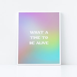 Könnte beinhalten: Ein weißer gerahmter Druck mit einem Regenbogen-Verlaufshintergrund und dem Text "WHAT A TIME TO BE ALIVE" in Weiß.